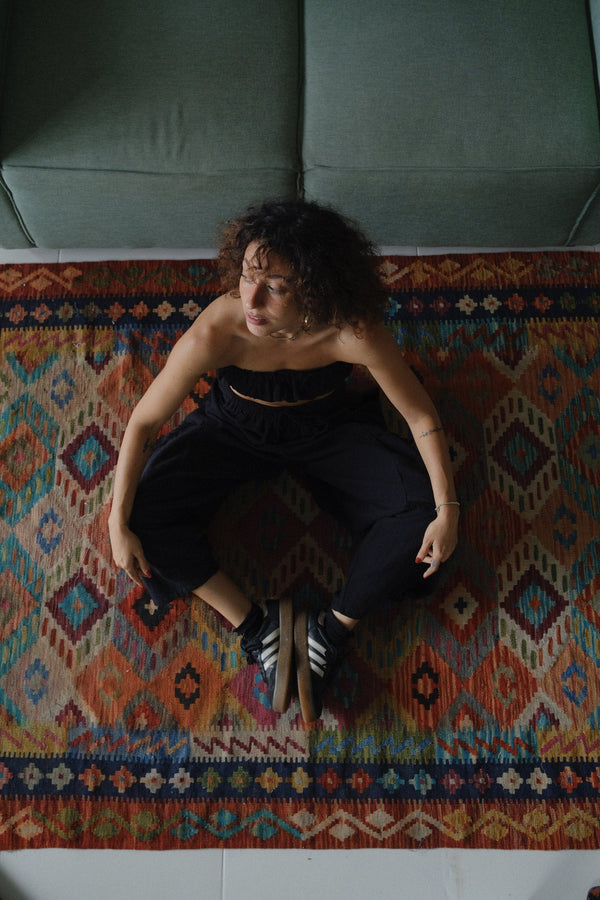 Seated in loose black cotton on a Balinese rug
