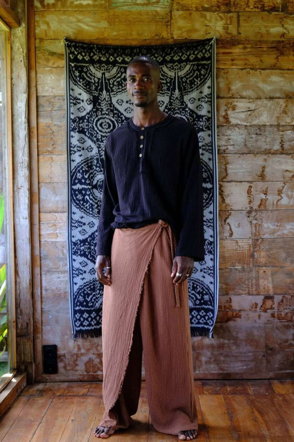 Model wearing Nahara Pants Brown - Men with a black shirt, showcasing relaxed summer fashion in a tropical setting.