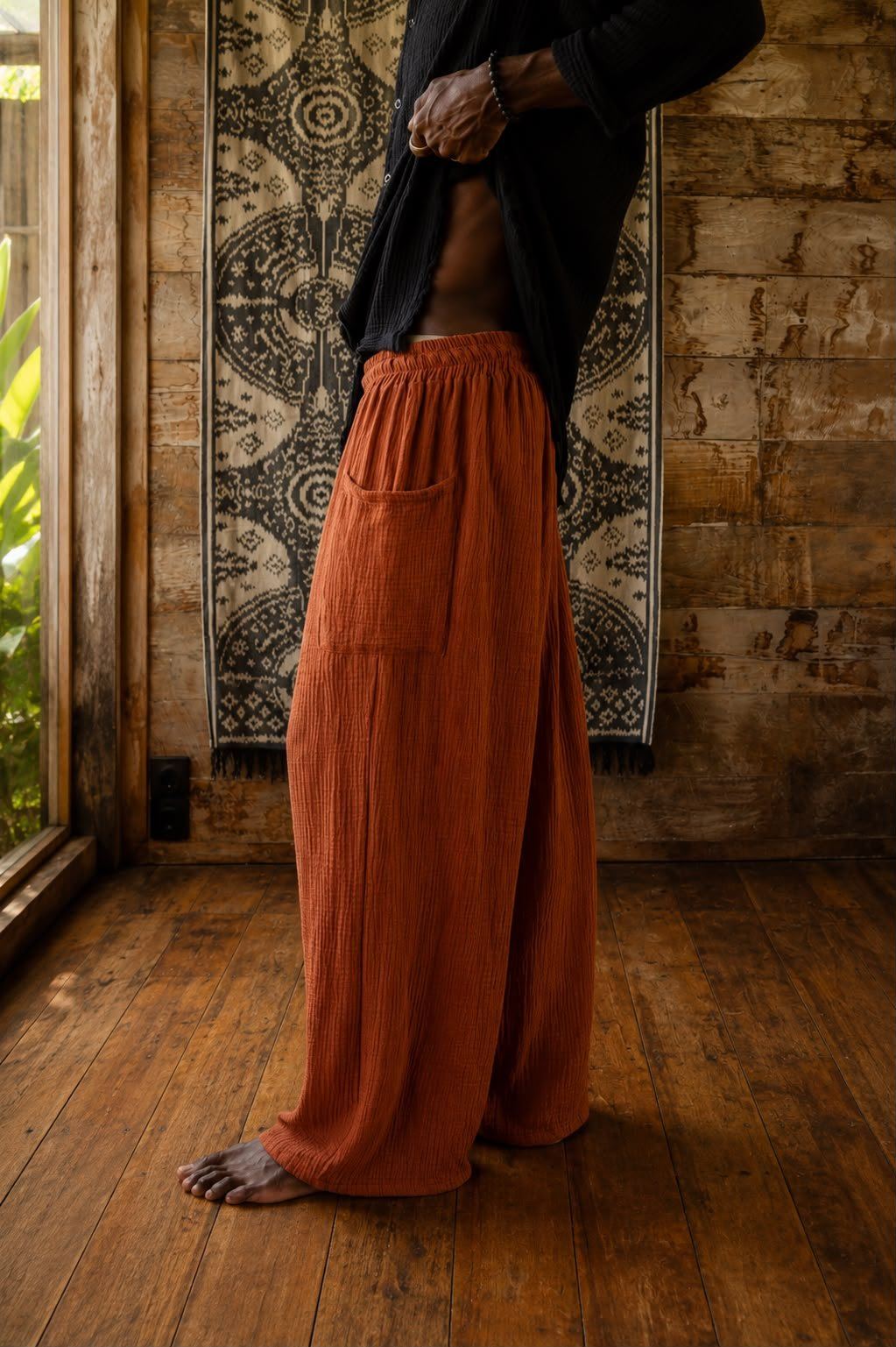 Terracotta crinkle-cotton wide-leg pants from SNUG, worn in a wooden Bali interior